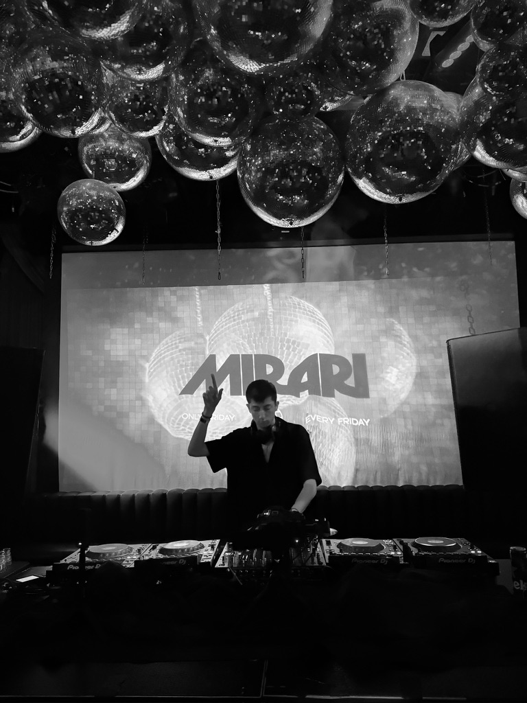 Black-and-white portrait of Mathéos performing beneath mirrored disco balls